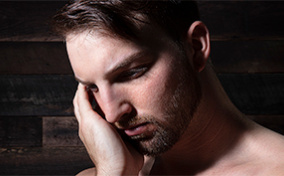 A man rubs his face while looking downward.