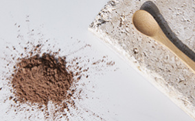 A wooden spoon on a stone plate lies next to a pile of brown powder.