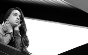 A woman rests her chin in her hands as she looks out from a balcony railing. 