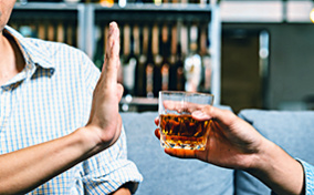 A man holds his hand up to refuse an alcoholic drink being offered to him.