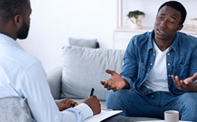 A man talks to his therapist with his arms shrugging and palms up.